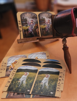 Photo d'un stéréoscope sur une table de bois. Quelques photos sont empilées sur la table. L'une d'entre elles est installé dans le stéréoscope.