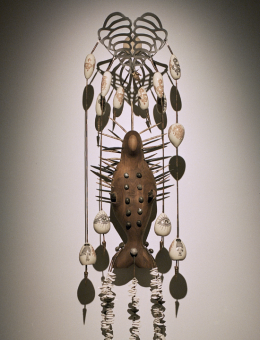 Photo d'une œuvre nommée L'archère. On y voir une sculpture murale comprenant du bois, de la céramique et du métal. 